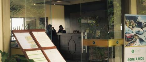 A reception desk with a glass partition, a signboard with text, and a poster advertising a ride service.