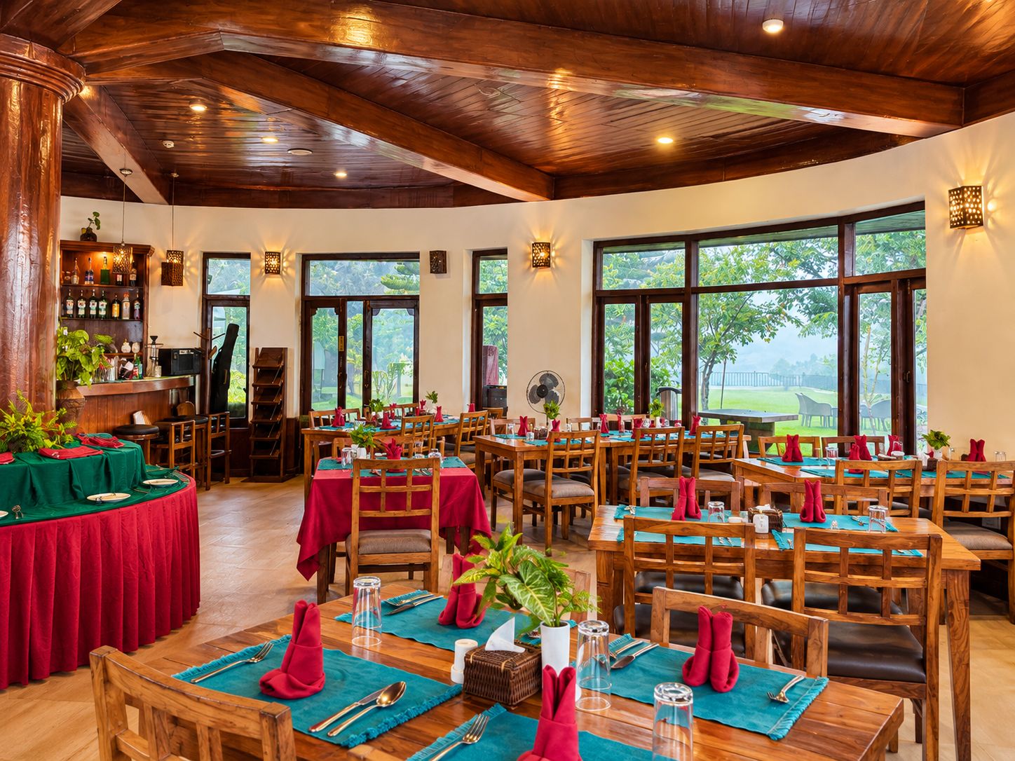 A restaurant with multiple tables set for dining, wooden furniture, and large windows offering a view of the outdoors.