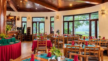 A restaurant with multiple tables set for dining, wooden furniture, and large windows offering a view of the outdoors.