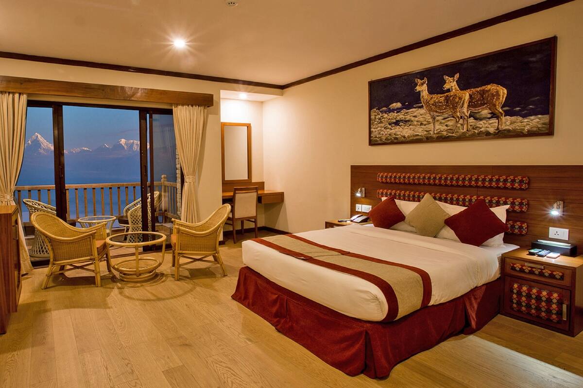 A hotel room with a large bed, a desk, a chair, and a balcony with a view of the mountains.