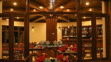 A restaurant with a long table set for a meal, wooden walls, and a bar area visible through the windows.