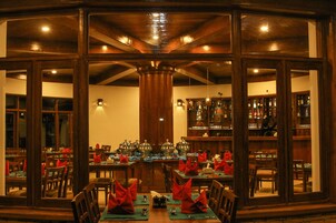 Un restaurante con una larga mesa dispuesta para una comida, paredes de madera y una zona de bar visible a través de las ventanas.