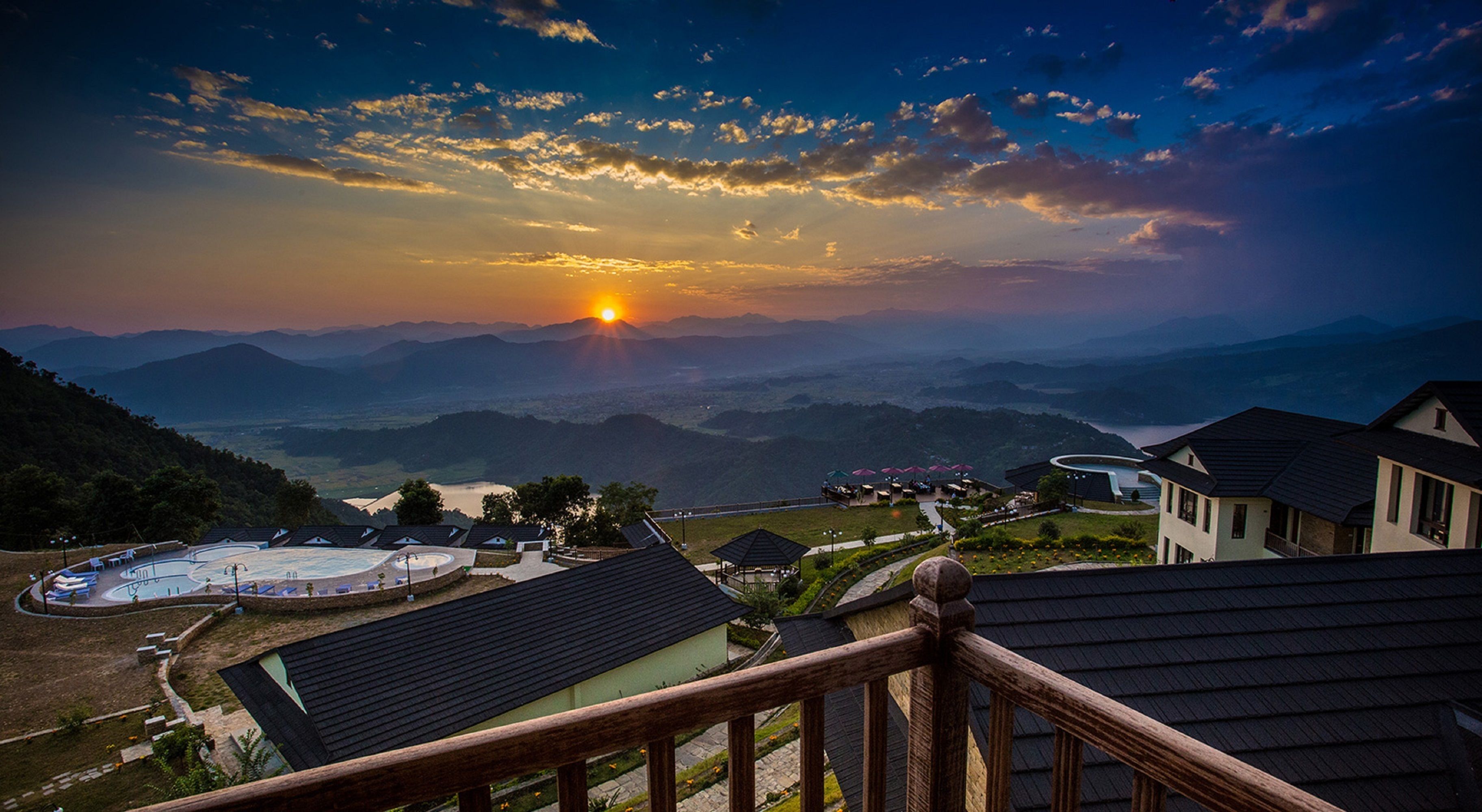 A resort with a pool, multiple buildings, and a view of the sunset over mountains.