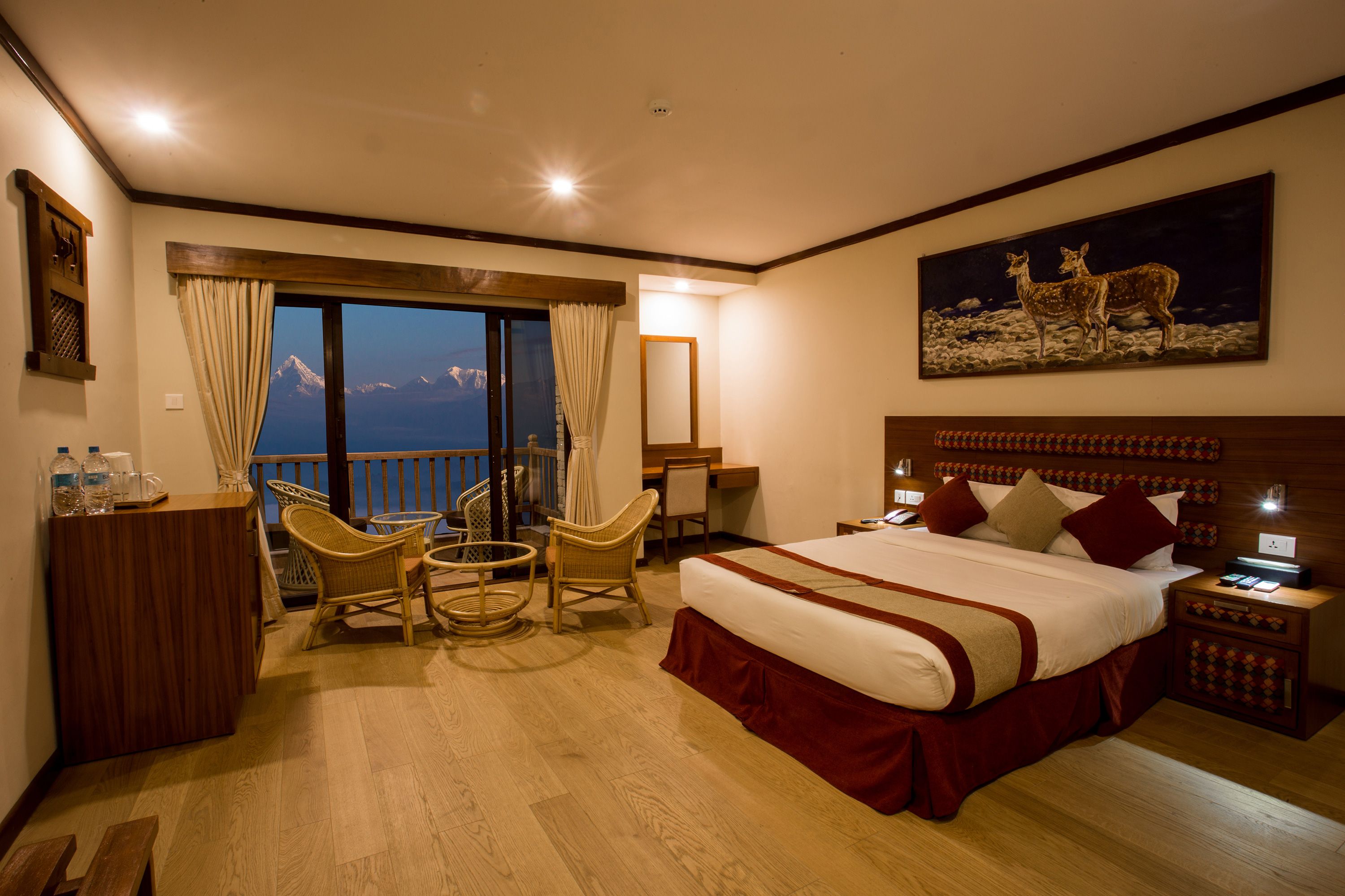 Une chambre d’hôtel avec un lit, un bureau, une chaise, une petite table, un balcon avec des rideaux et un tableau au mur.