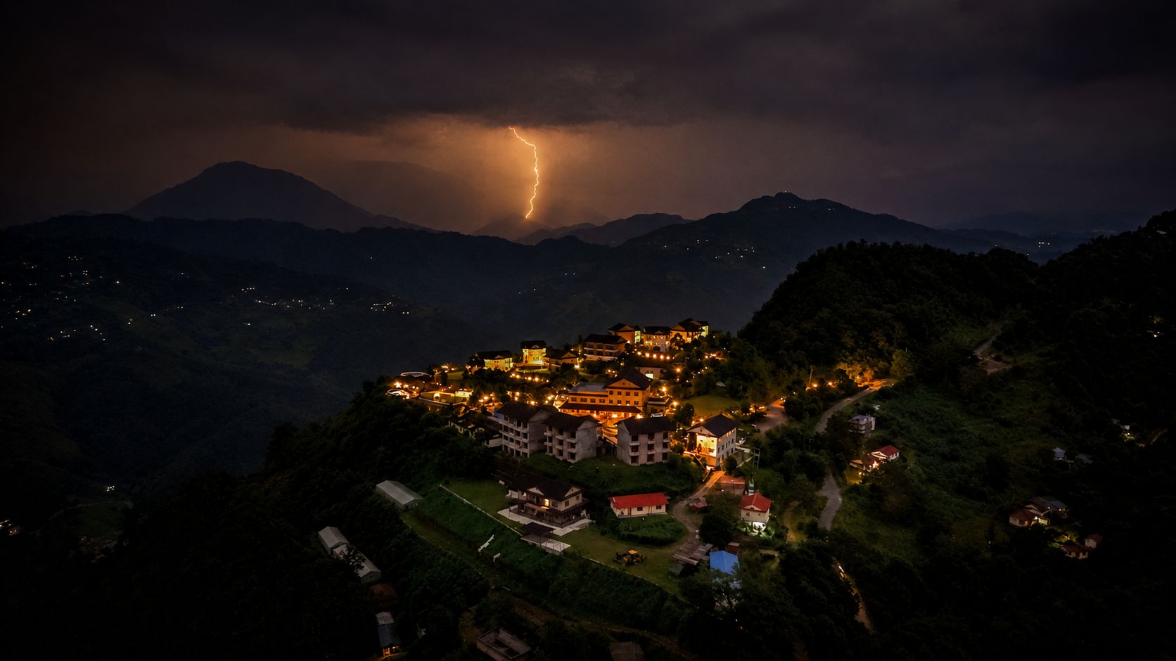 A mountainous town at night with a lightning strike.
