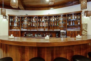 A bar area with wooden shelves stocked with liquor bottles and glasses, a coffee machine, and a tissue box.
