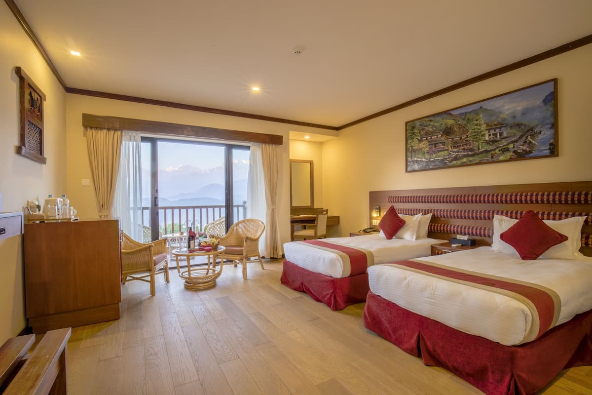 A hotel room with two beds, a desk, a chair, a balcony with a view of mountains, and a painting on the wall.