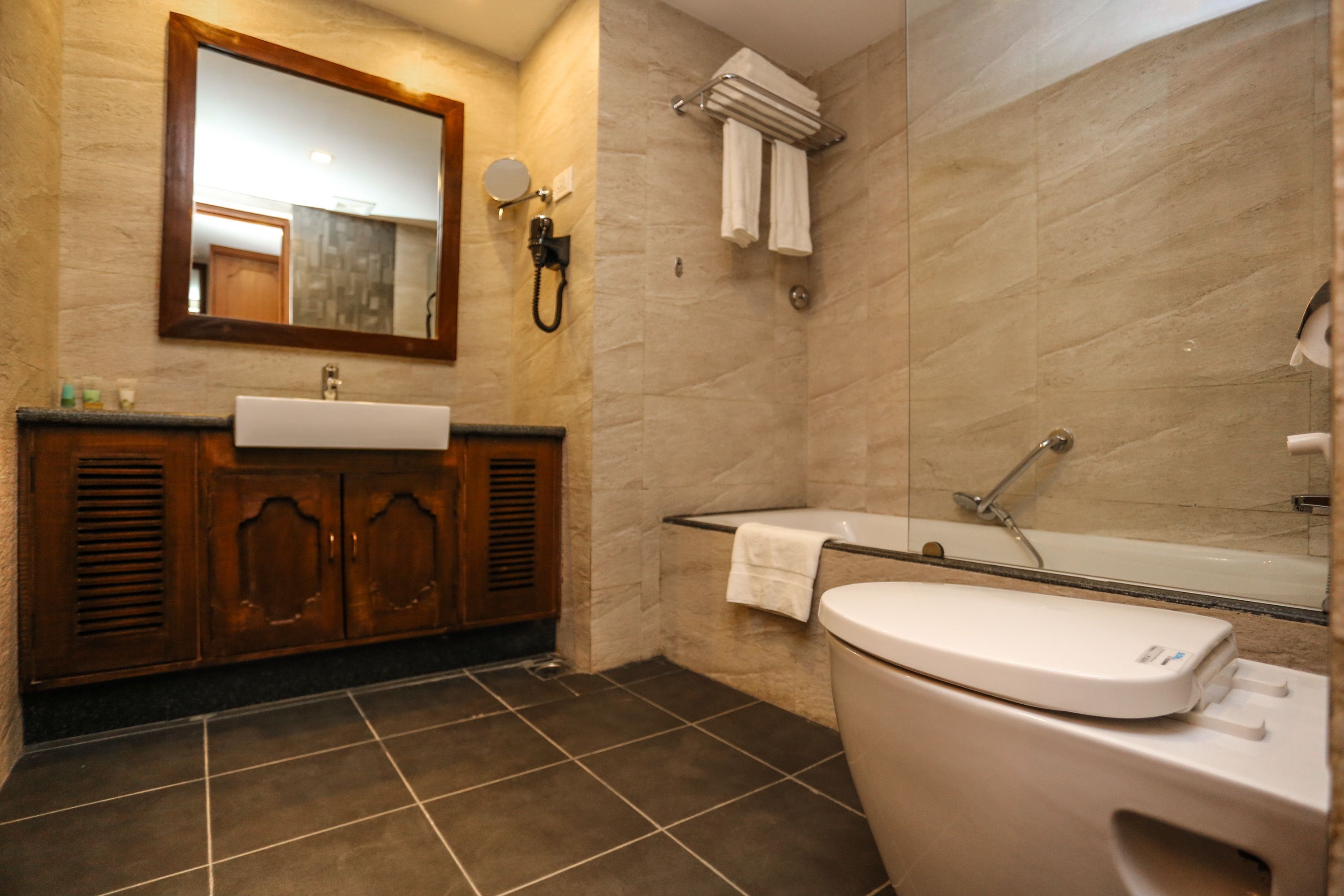 A bathroom with a wooden vanity, a sink, a toilet, a shower, and a large mirror.