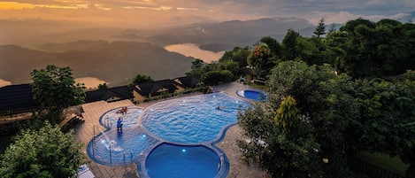 A resort with multiple swimming pools surrounded by lush greenery and a view of distant mountains.