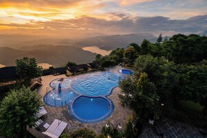 Un resort con varias piscinas rodeado de exuberante vegetación y vistas a montañas distantes.