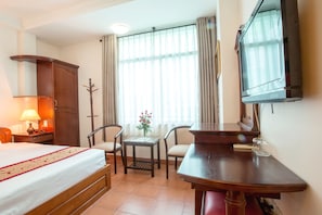 A hotel room with a bed, a desk, a chair, a television, and a window with curtains.