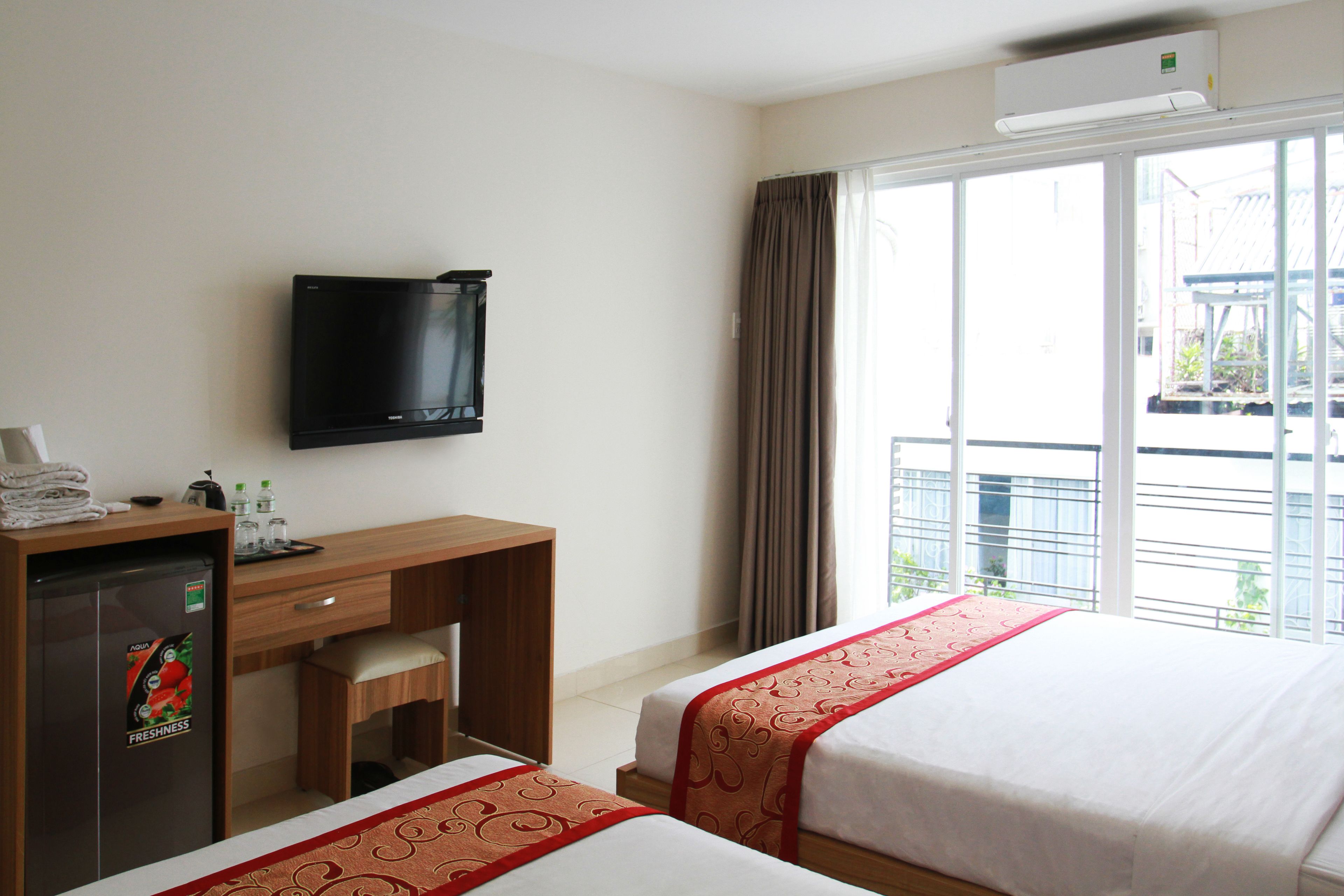 Quarto de hotel com cama, escrivaninha, televisão e janela com cortinas.