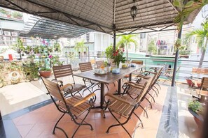 An outdoor patio with a table and chairs, surrounded by potted plants and a view of the city.