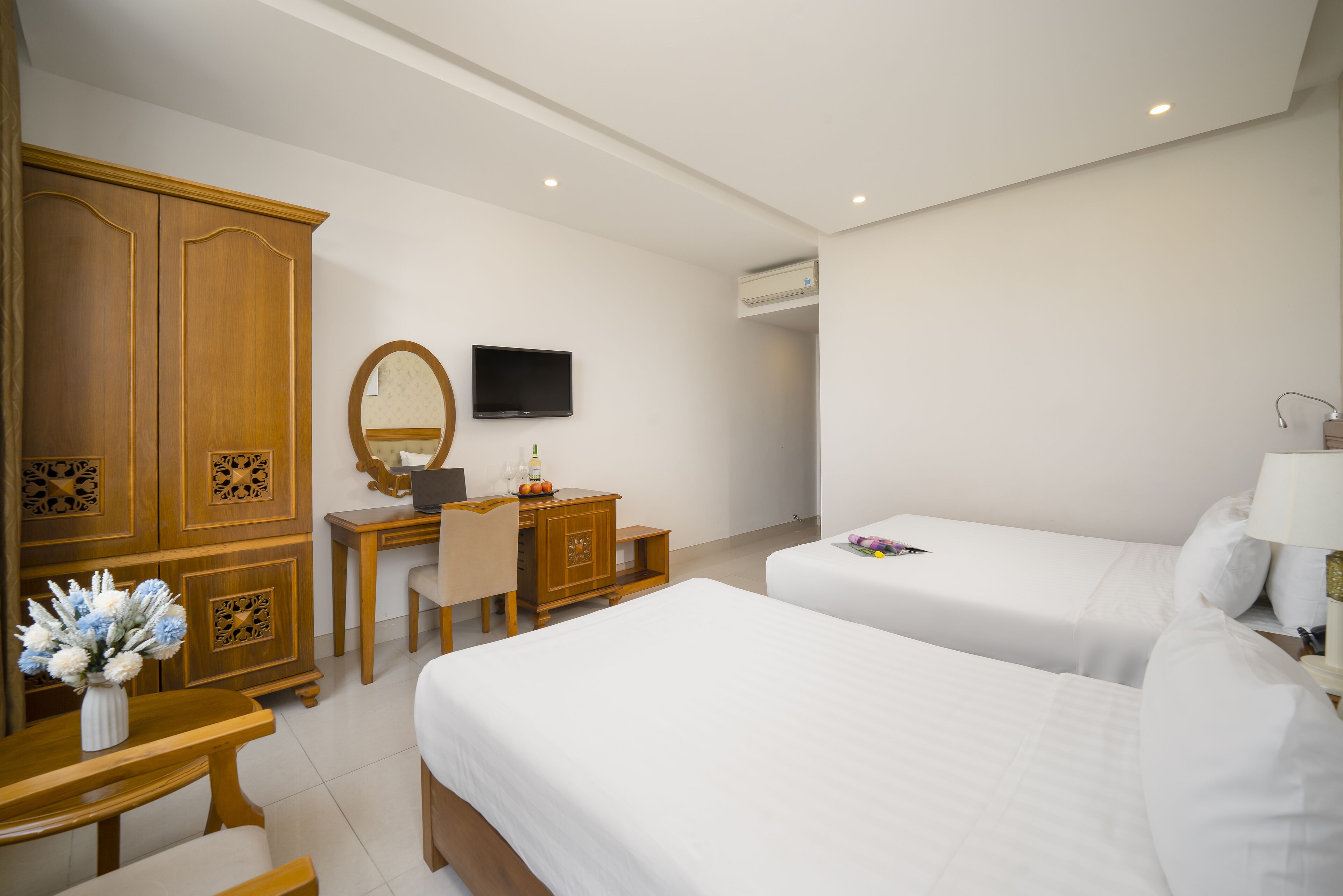 Une chambre d’hôtel avec deux lits, un bureau avec une chaise, une armoire, une télévision et un miroir.
