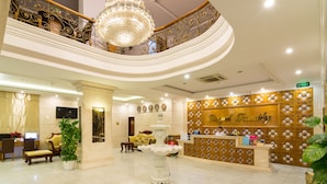 A hotel lobby with a reception desk, a chandelier, a fountain, and a staircase. - Royal Family Hotel Da Nang (Da Nang)