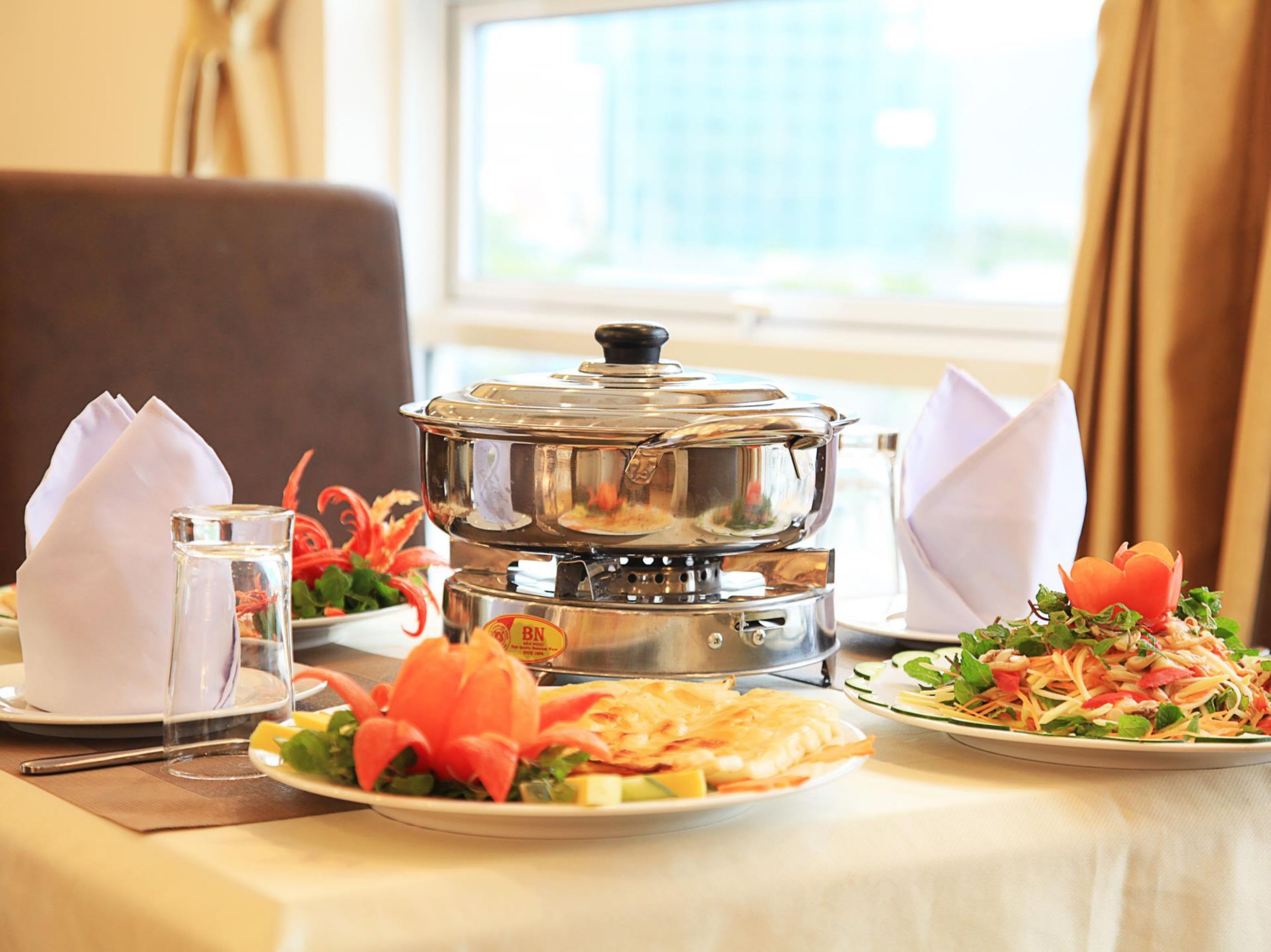 A dining table with a pot, two plates of food, a glass of water, and a napkin.