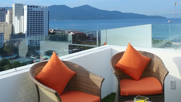 A balcony with wicker chairs and a glass table, overlooking a cityscape and the sea. - Royal Family Hotel Da Nang (Da Nang)