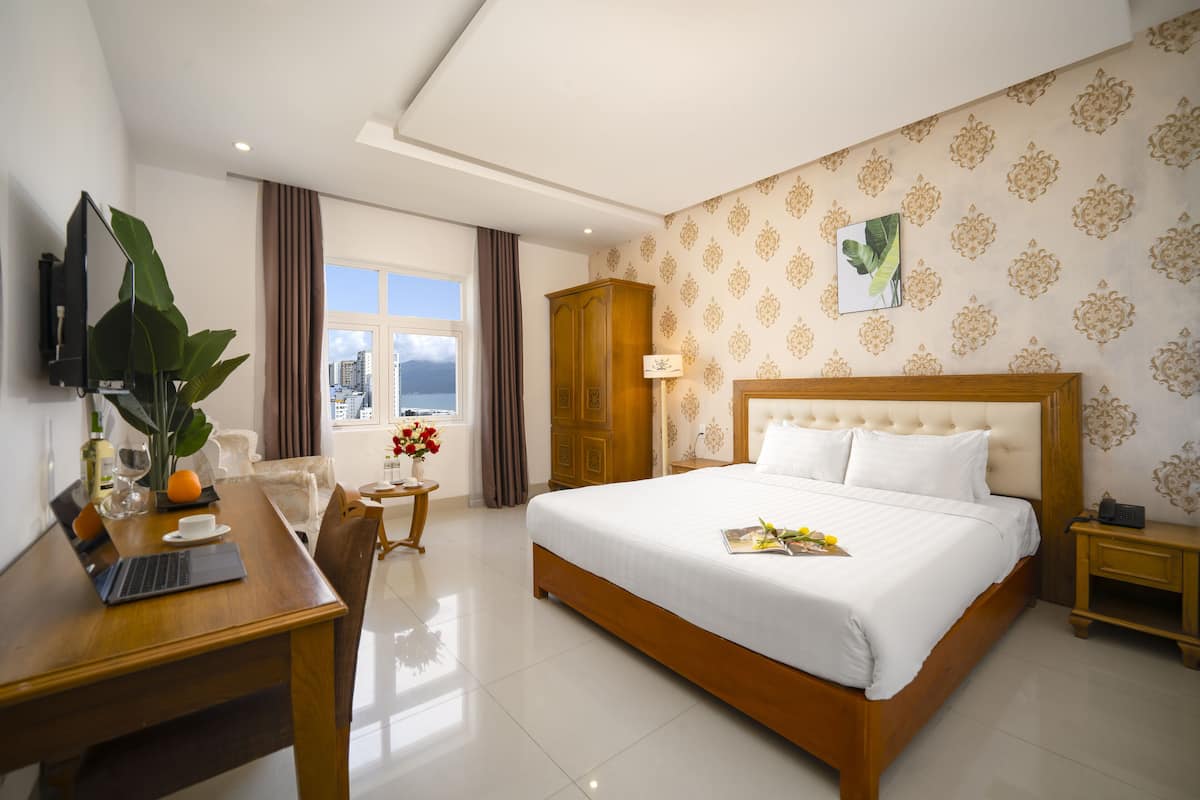 A hotel room with a large bed, a desk with a laptop, a TV, and a view of the city through the window.