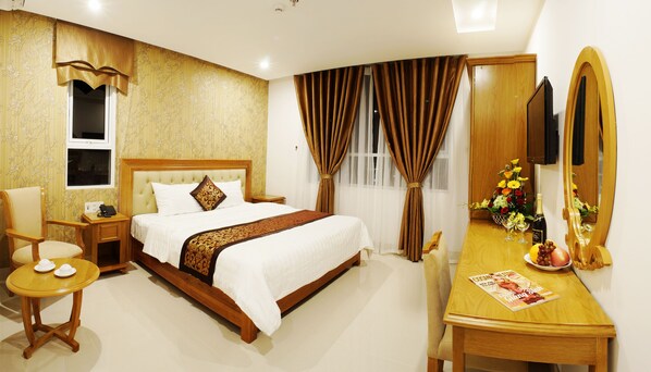 A hotel room with a bed, a wooden desk, a chair, a small table, a mirror, and a window with curtains. - Royal Family Hotel Da Nang (Da Nang)