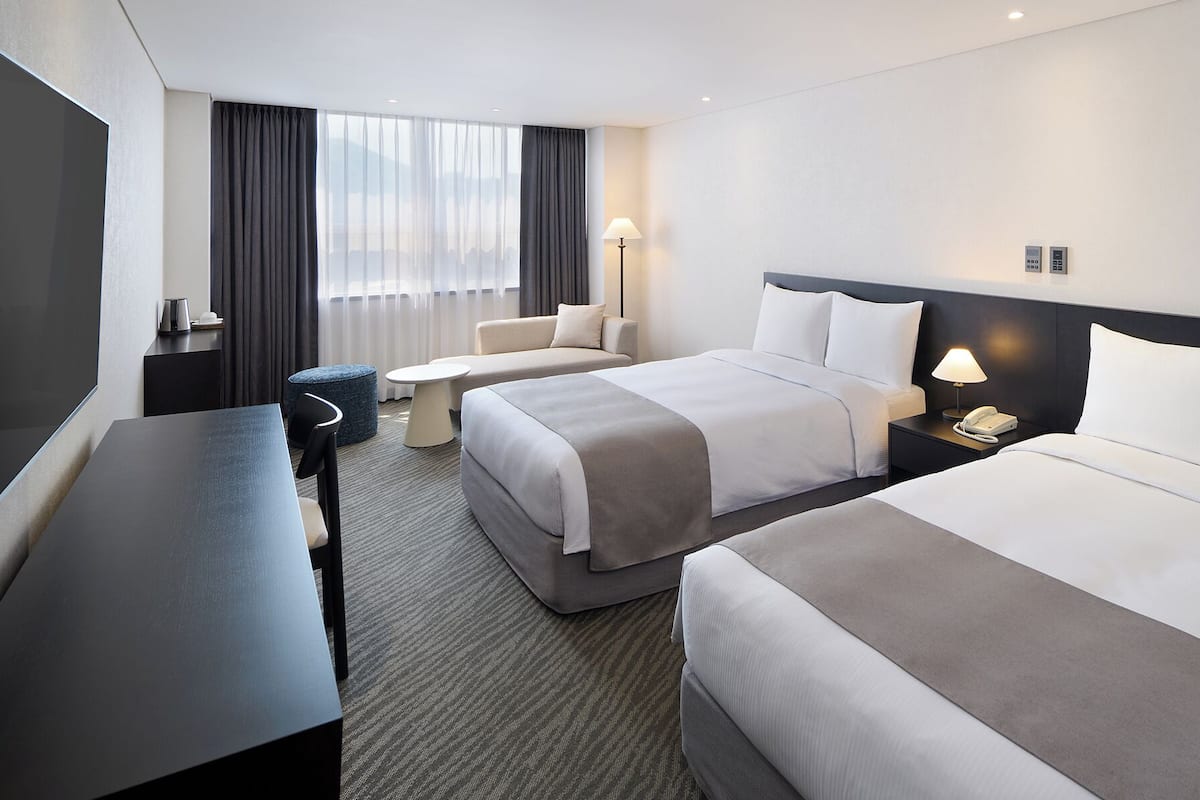 A hotel room with two beds, a desk, a chair, a lamp, and a phone on the nightstand.