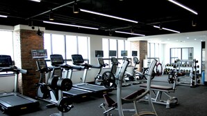 A gym with various exercise equipment, large windows, and a brick wall. - Hotel President (Seoul)