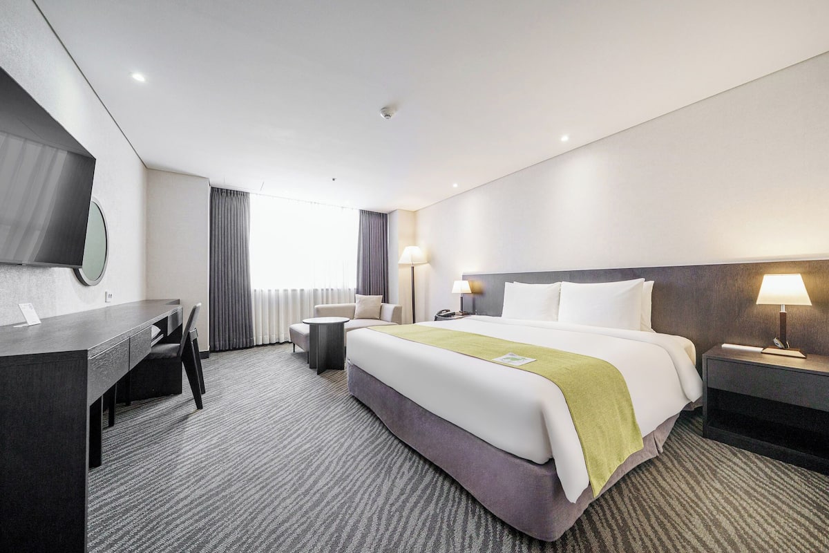 A hotel room with a bed, desk, chair, lamp, and a television.
