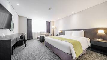 Habitación de hotel con cama, escritorio, silla, lámpara y televisor.