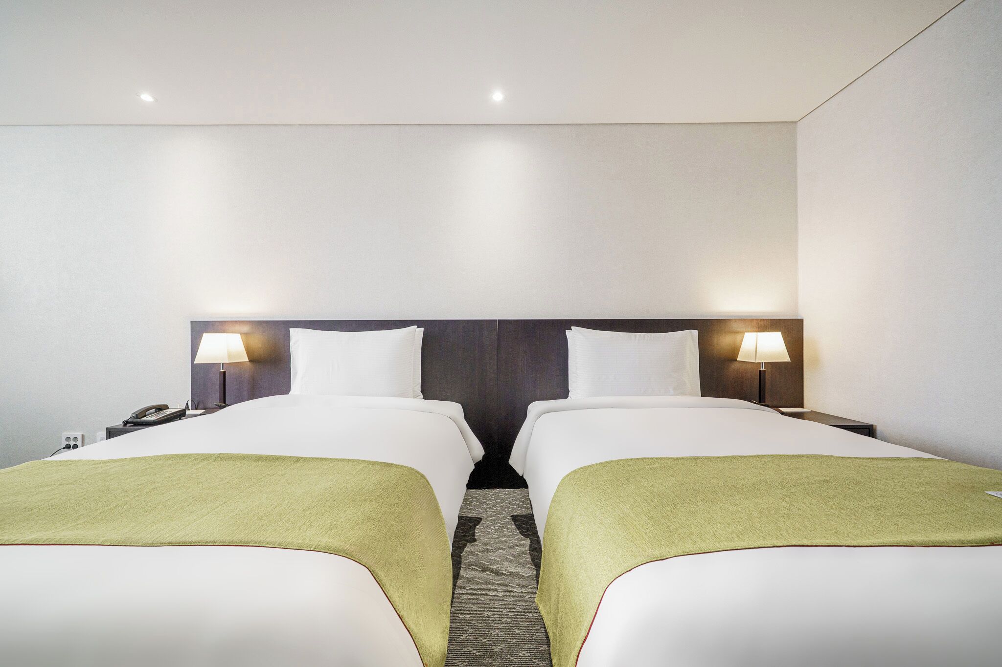 A hotel room with two beds, a nightstand with a lamp, and a telephone.