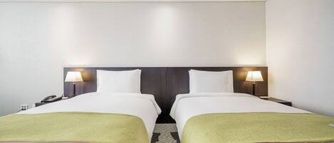 A hotel room with two beds, a nightstand with a lamp, and a telephone.