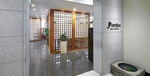 A reception area with a polished floor, a wooden partition with a grid design, and a stone wall with a logo. - Hotel President (Seoul)