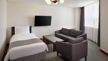 A hotel room with a bed, a sofa, a coffee table, and a flat-screen TV mounted on the wall.
