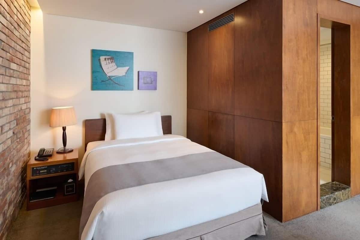 A hotel room with a large bed, a nightstand with a lamp, a brick wall, and a wooden panel wall.