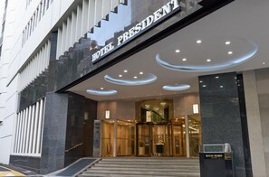 A modern hotel entrance with a revolving door, a sign reading 'HOTEL PRESIDENT,' and a reception desk. - Hotel President (Seoul)