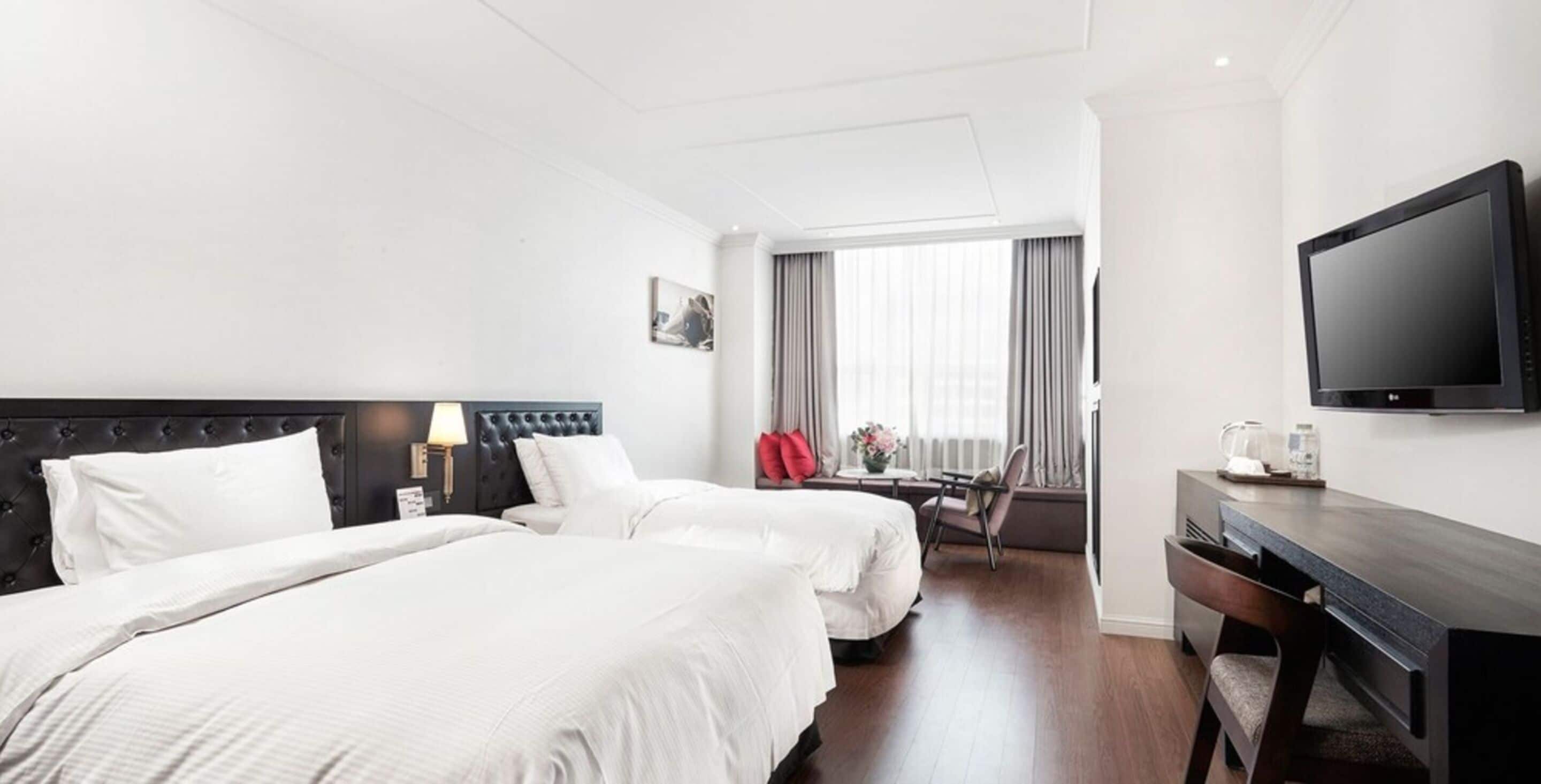 A hotel room with two beds, a desk, a chair, a television, and a window with curtains.