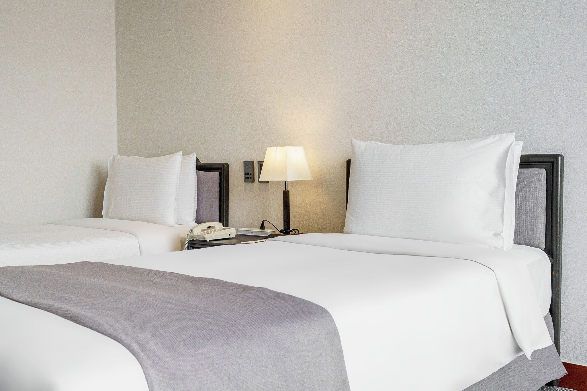 Habitación de hotel con cama, mesita de noche, lámpara y teléfono.