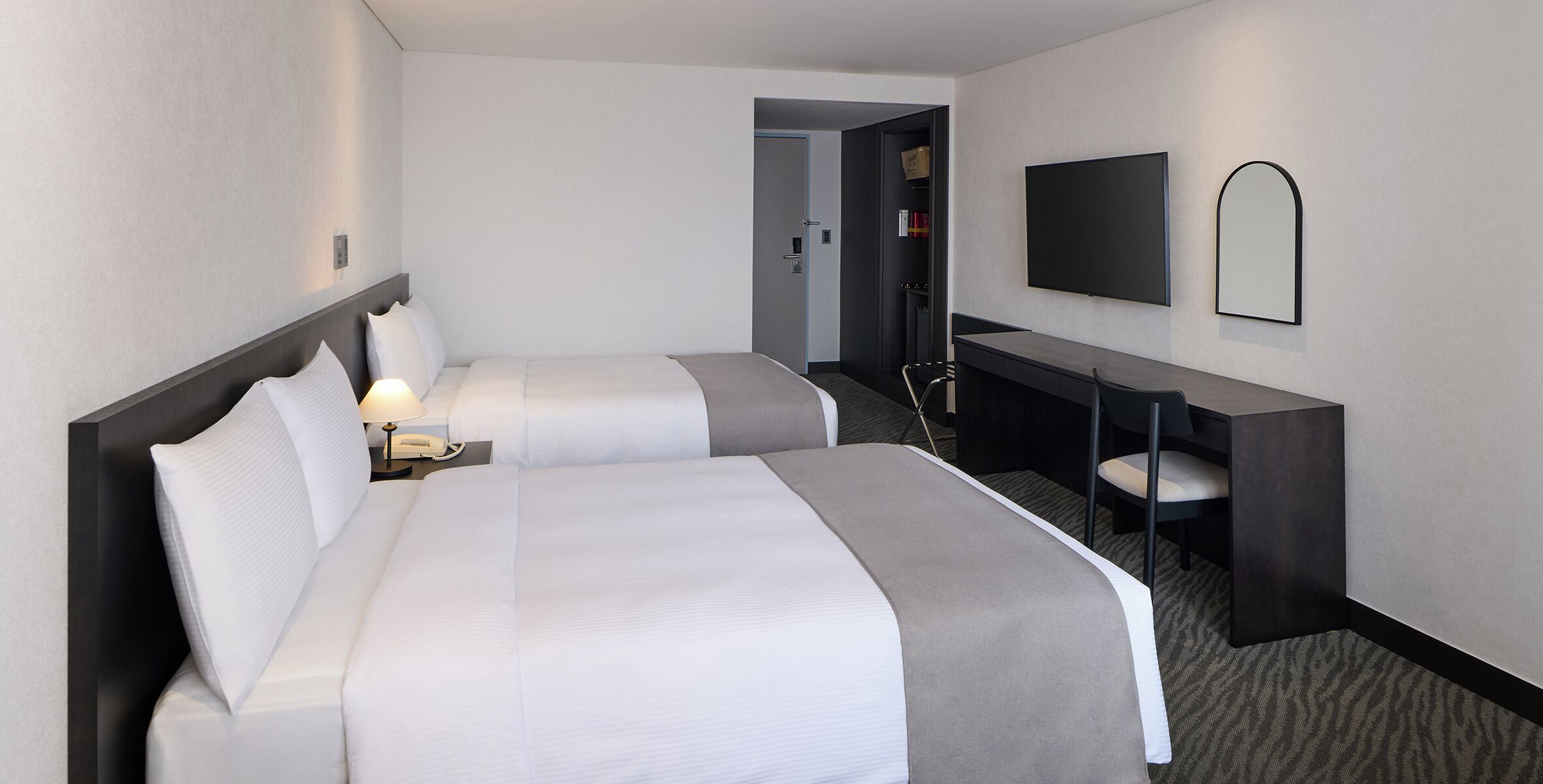 A hotel room with two beds, a desk, a chair, a TV, and a mirror.