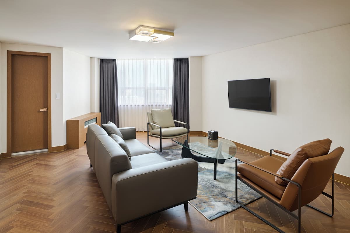 A modern living room with a sofa, armchair, glass coffee table, and a flat-screen TV mounted on the wall.