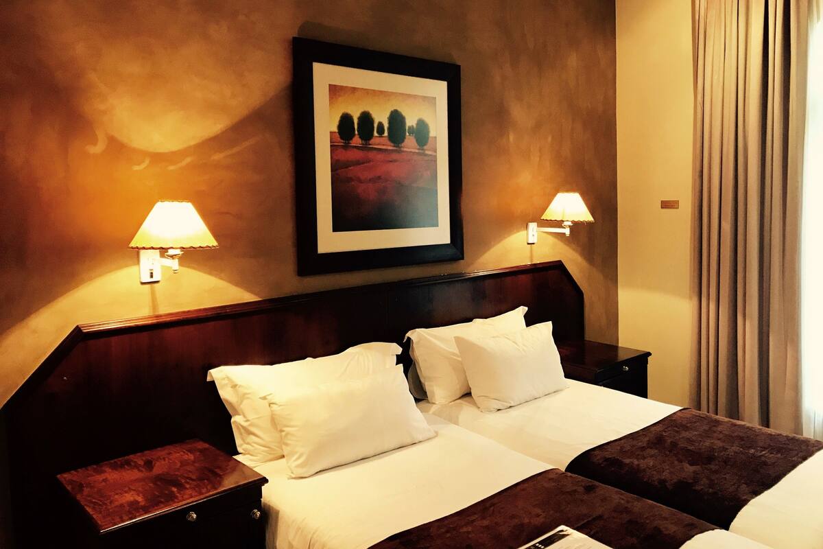 A hotel room with a large bed, two bedside tables, a headboard, and two wall-mounted lamps.