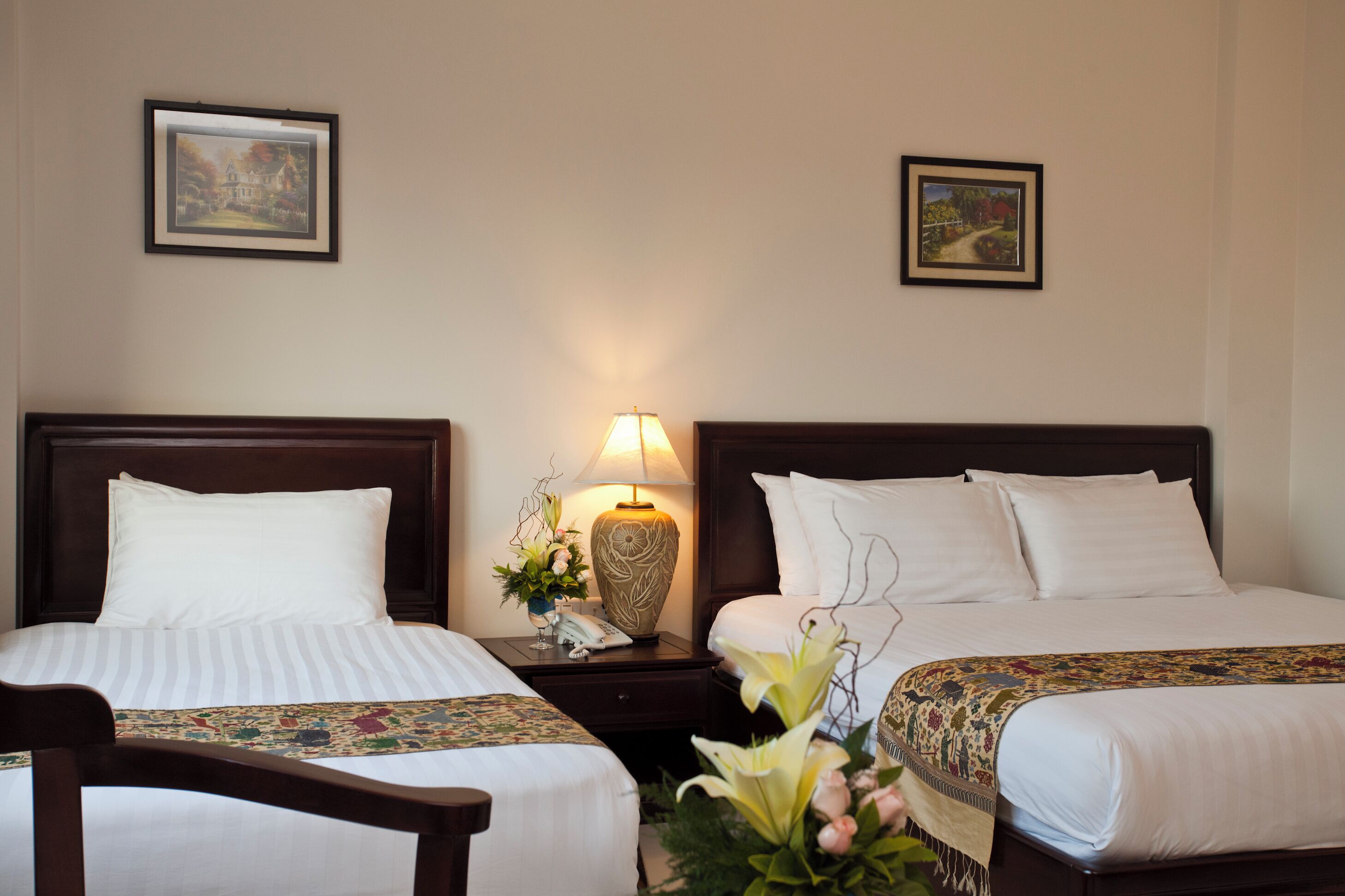 Una habitación de hotel con dos camas, una mesita de noche con lámpara y cuadros en la pared.