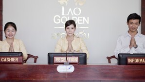 Three individuals seated at a reception desk with nameplates reading "CASHIER," "RECEPTION," and "INFORMA." - Lao Golden Hotel (Vientiane)