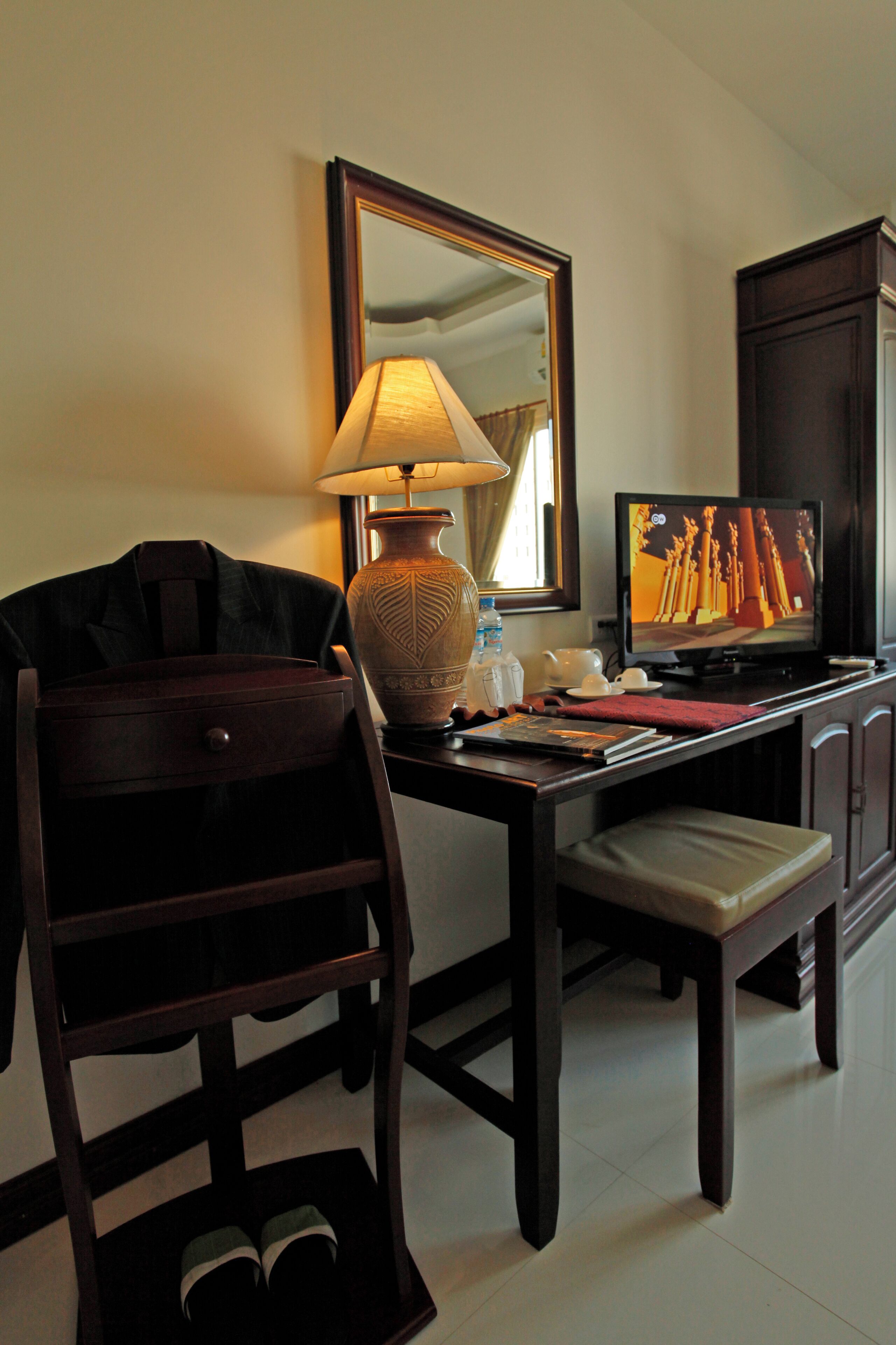 A hotel room with a wooden desk, a television, a lamp, a mirror, and a chair.