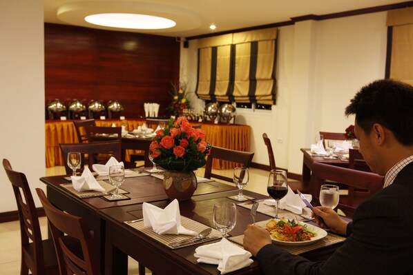 A dining table set with plates, glasses, and a vase of flowers. - Lao Golden Hotel (Vientiane)