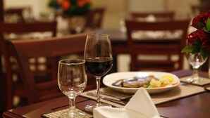 A dining table with two wine glasses, one filled with red wine, and a plate of food. - Lao Golden Hotel (Vientiane)