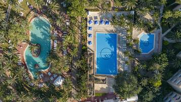 Vista aérea de un complejo turístico con múltiples piscinas, tumbonas y palmeras.