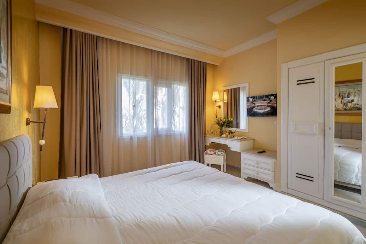 Ein Hotelzimmer mit einem großen Bett, einem Schreibtisch mit Stuhl, einem Kleiderschrank und einem Fenster mit Vorhängen.