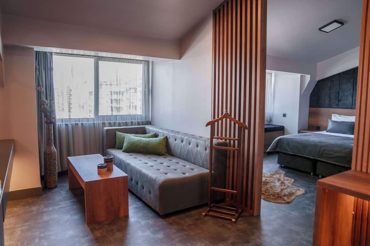 Een moderne hotelkamer met een bank, een houten salontafel, een kapstok en een bed met een donkere hoofdbord.