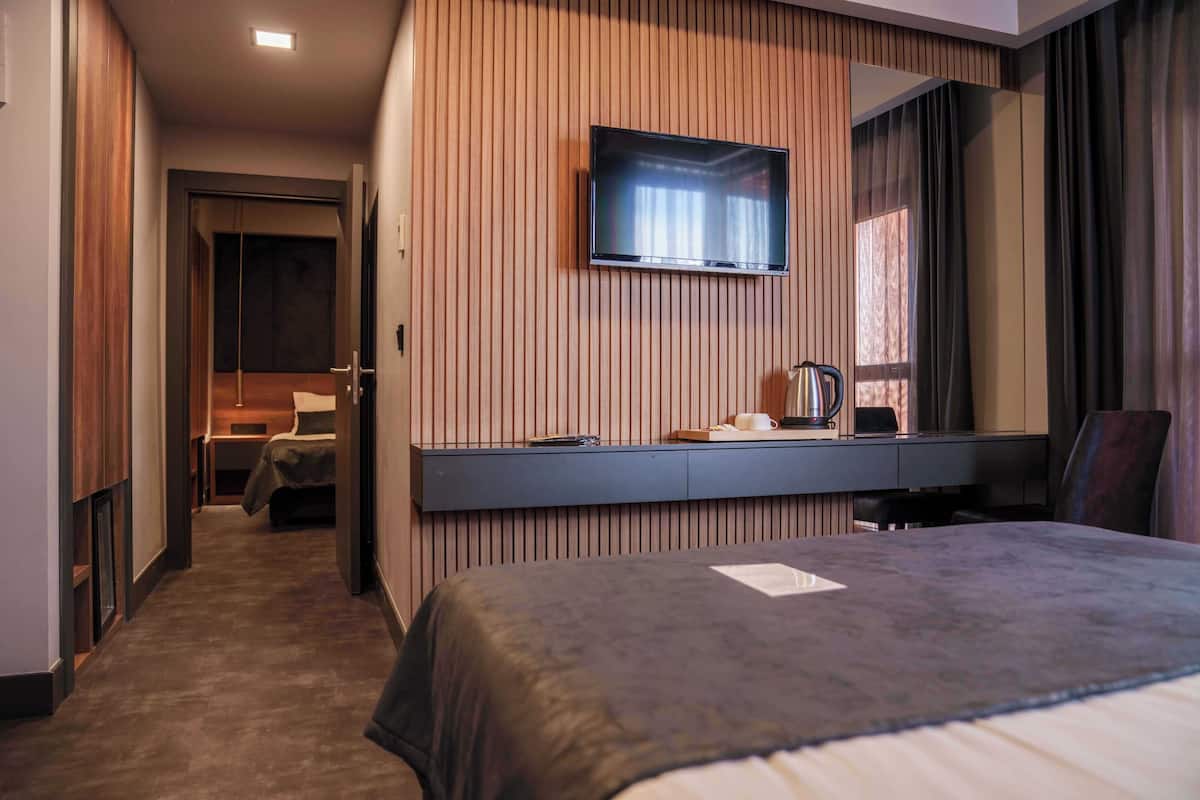 Een hotelkamer met een bed, een aan de muur bevestigde televisie, een bureau met stoel, en een raam met gordijnen.