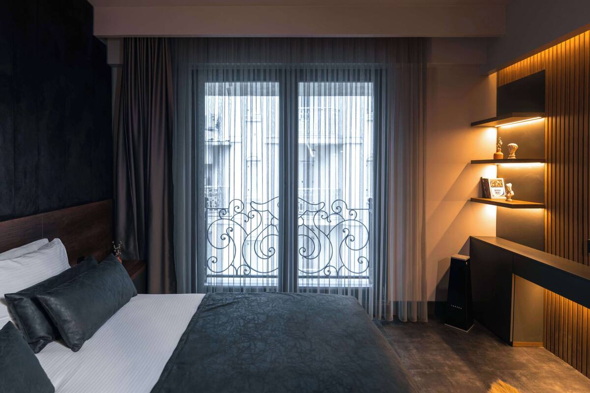 Een moderne hotelkamer met een groot bed, een bureau met lamp en uitzicht door een raam met een sierijzeren hek.