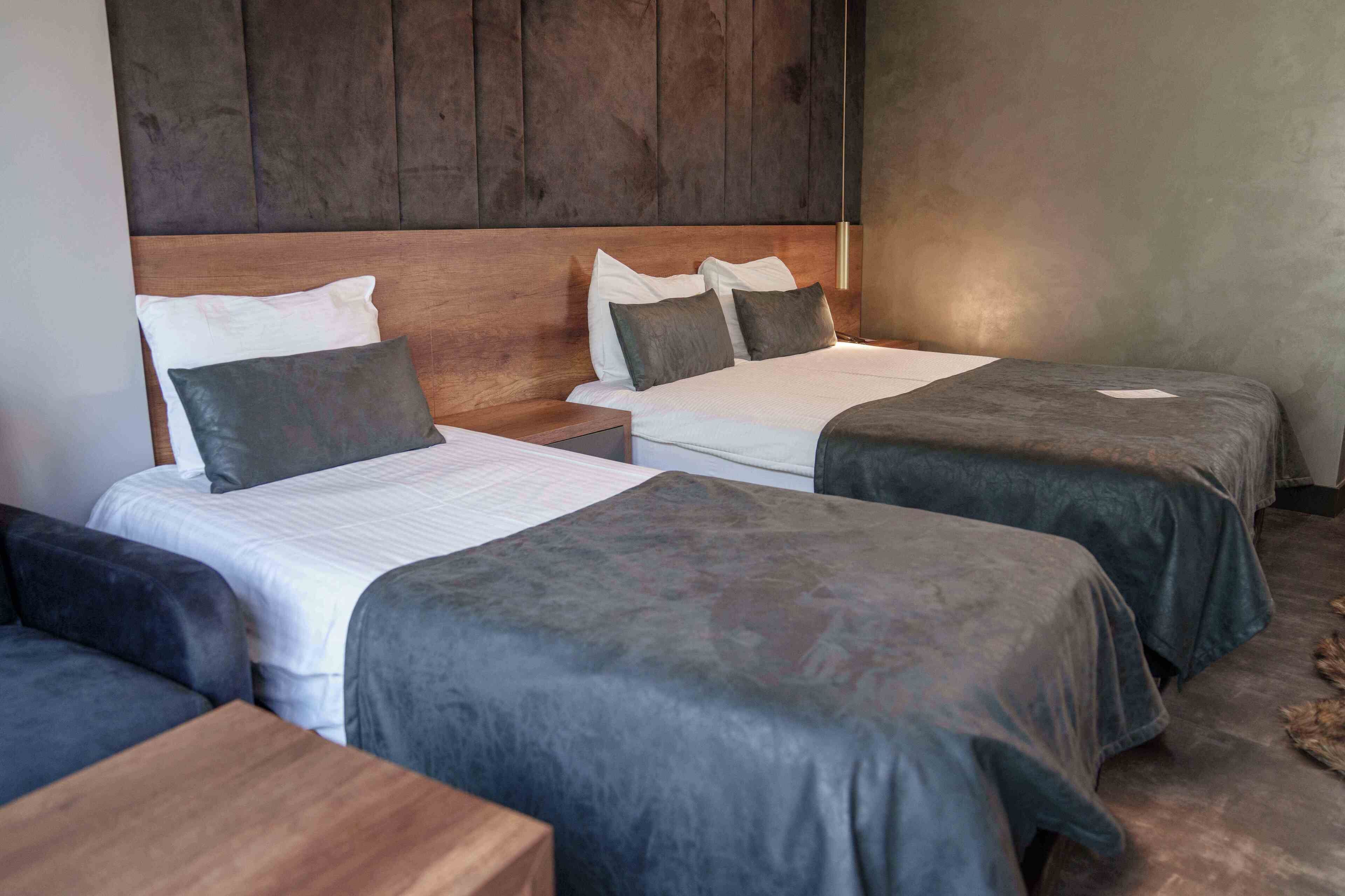 Ett hotellrum med två sängar, var och en med en sänggavel i trä och grått sänglinne. Mellan sängarna står ett litet nattduksbord i trä, och längre fram i rummet finns ett litet bord.