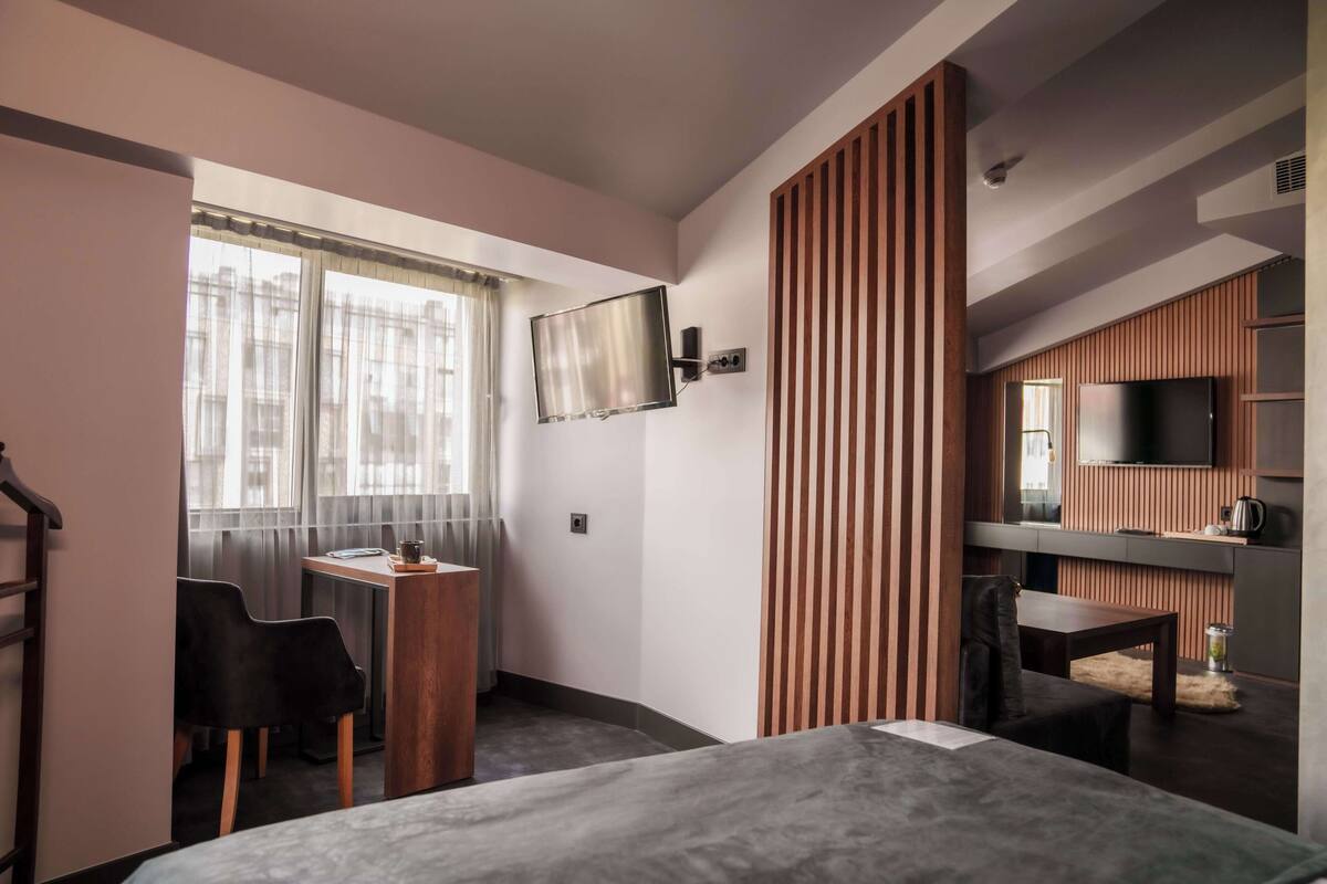 Een moderne hotelkamer met een bed, een bureau met stoel, een aan de muur bevestigde televisie en een kitchenette.